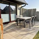 Terrasse mit Tisch, Stühlen und Sonnenschirm. Hinterhof mit Holzzaun.