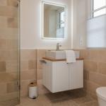 Badezimmer mit Dusche, Waschbecken und Toilette. Fliesenwand und Spiegel mit Beleuchtung.