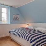 Schlafzimmer mit Bett, Fenster und Wandbild. Holzfußboden und blaue Wände.