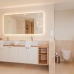 Badezimmer mit Doppelwaschbecken, beleuchtetem Spiegel und Toilette.