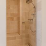 Dusche mit Glaswand, Steinfliesen und Handbrause.