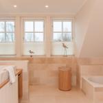 Badezimmer mit Badewanne, Waschbecken und drei Fenstern mit Jalousien.