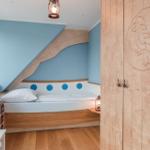 Schlafzimmer mit Bett unter Dachschräge, Holzschränkchen und Fensterbank.