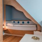 Schlafzimmer mit Bett unter Dachschräge, Holzmöbel und blauer Wand.