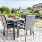 Garten mit Tisch und Stühlen auf gepflastertem Platz. Hintergrund mit Grünflächen und Häusern.