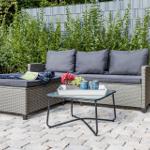 Garten mit grauem Rattan-Sofa und Tisch mit Blumen.