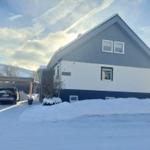 Wohnhaus mit Schneebedecktem Dach und weißer Fassade. Auto parkiert unter Carport.
