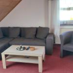 Wohnzimmer mit grauem Sofa, Sessel und Holztisch. Holzdecke und Fenster mit Vorhängen.