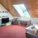 Wohnzimmer mit Holzdecke, Fernseher, Sofa und Sessel. Fenster mit Blick nach draußen.