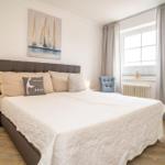 Schlafzimmer mit Bett, Wandbild und Fenster mit Vorhängen.