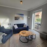 Wohnzimmer mit Sofa, Sessel und runden Tischen. Durchgang zur Terrasse.