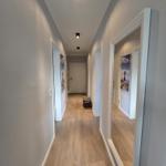 Flur mit Holzboden und Türen zu Räumen, Wandbilder und Deckenleuchten.