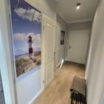 Flur mit Holzboden, Wandbild Leuchtturm und Haken. Tür zu Wohnraum und Bad.