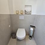 Toilette mit Wandhalterung, Toilettenbürste und dekorativen Objekten.