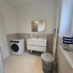 Badezimmer mit Waschmaschine, Waschtisch und Spiegel.