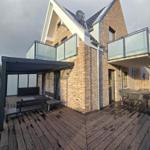 Haus mit Holzterrasse, Glasbalcony und Außensitzgelegenheiten.