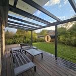 Terrasse mit Holzdecke, Sitzgelegenheiten und Garten mit Sauna.