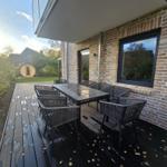Terrasse mit Tisch und Stühlen, dunkler Holzboden, Backsteinwand und großes Fenster.