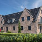 Modernes Haus mit Ziegelfassade und Balkon. Garten mit Beete und Bäumen.