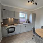 Küche mit Essbereich, graue Schränke, Holztisch und Fenster.