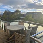 Terrasse mit Rattan-Tisch und Stühlen, Blick auf Wohnhäuser und Bäume.