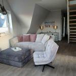 Wohnzimmer mit Sofa, Sessel und Holzboden unter Dachschrägen.