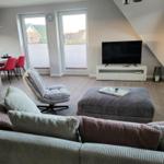 Wohnzimmer mit Sofa, Sessel, Fernseher und Fenstern.