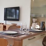 Esstisch mit Stühlen, Küchenzeile und Fernseher an der Wand.