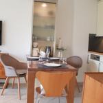 Essbereich mit Tisch, Stühlen und Fernseher. Küche mit weißen Schränken und Arbeitsplatte.