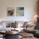 Wohnzimmer mit Sofa, Sessel und Tisch. An der Wand hängen zwei Bilder.