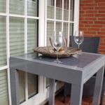 Terrasse mit Tisch, Stühlen und Weingläsern vor Fenster und Backsteinwand.