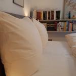 Schlafzimmer mit Bett, Kissen und Bücherregal an der Wand.