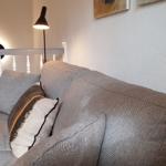 Ein grauer Sofa mit Kissen und Decke. Hintergrund mit Treppen und Lampen.