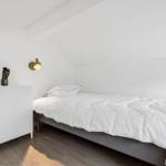 Bedroom with bed, nightstand, and wall lamp under sloped ceiling.