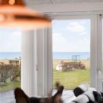 Large windows offer view of sea and lawn with outdoor table and chairs.