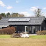 Black house with solar panels, terrace, and garden. Flag waving in the wind.
