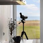 Telescope on tripod by window with view of landscape