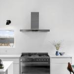 Modern kitchen with stainless steel stove and range hood. White countertops and window.