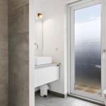 Bathroom with shower, sink, and toilet. Large glass door leads to balcony.
