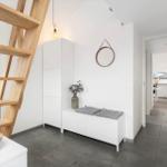 Entrance with wooden stairs, white cabinets, and gray floor. Hallway to the kitchen.