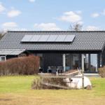 Black house with solar panels and terrace. Lawn and white boat in the foreground.