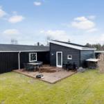 Schwarzes Haus mit Holzterrasse und Garten. Außentisch, Sitzgelegenheiten und Grillmöglichkeit.