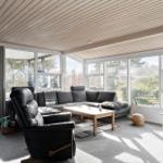 Wohnzimmer mit Sofa, Sessel und TV. Große Fenster und Holzdecke.