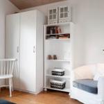 Schlafzimmer mit weißen Schränken, Sessel und Bücherregal.
