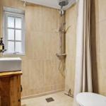 Bad mit Dusche, Waschbecken und Toilette. Fenster und Holzunterschrank sichtbar.