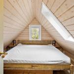 Schlafzimmer mit Holzwand und Dachschrägen, Bett mit weißer Matratze, Fenster und Dachfenster.