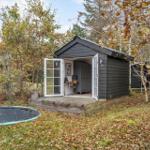 Ein kleines schwarzes Haus mit offenen Türen und einem Trampolin im Herbst.