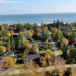 Aerial view of coastal village with houses among autumn trees and ocean in background.