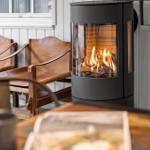 Ein Kamin mit brennendem Holz steht neben zwei Ledersitzen. Hintergrund: weiße Paneelen.