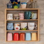 Wooden shelf with colorful mugs against brick wall